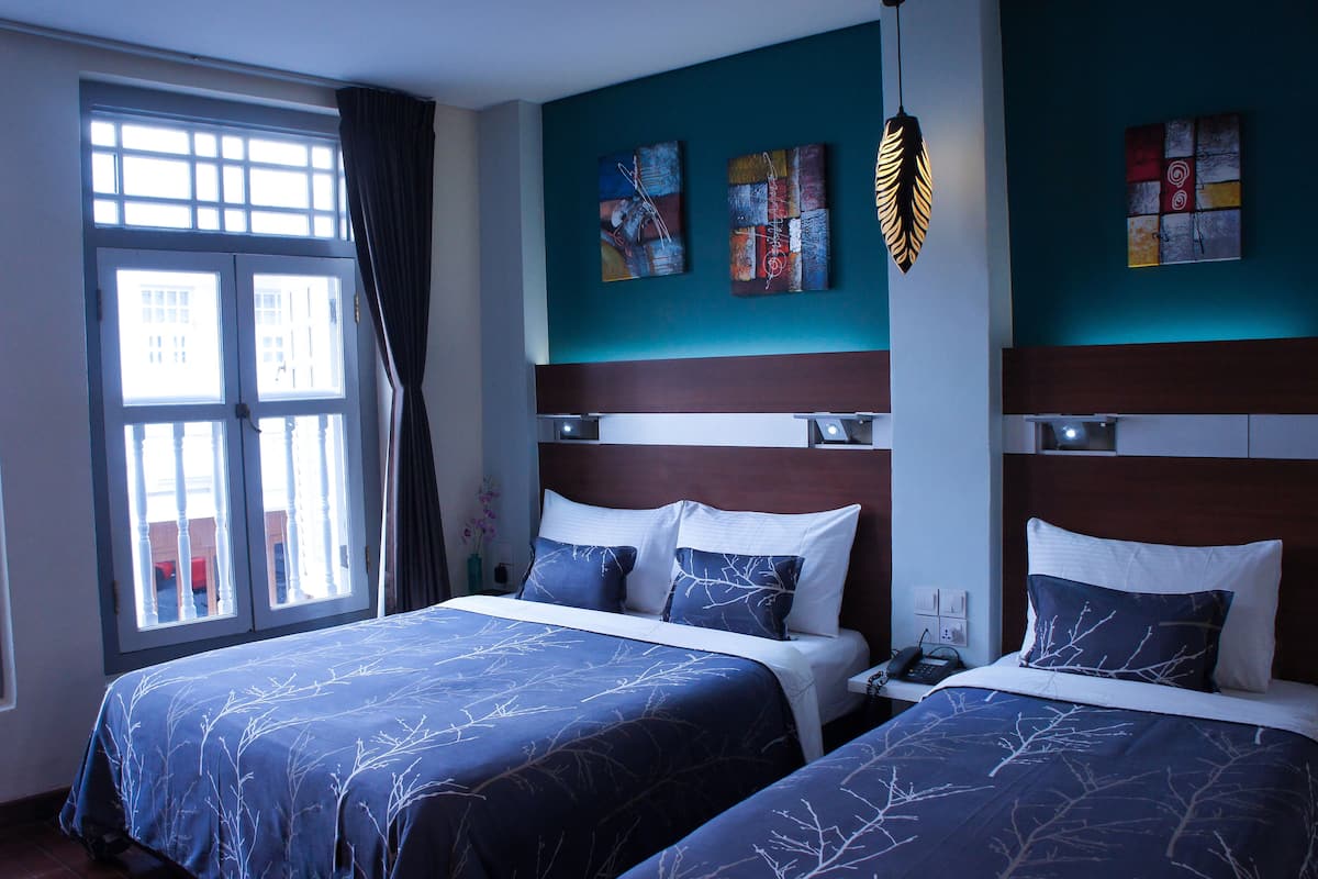 A hotel room with two beds, a large window with curtains, and artwork on the walls.