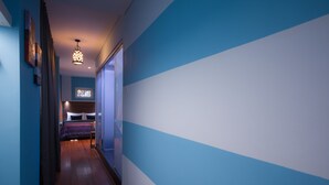 A hallway with a wooden floor, blue and white walls, and a bed with a blue and purple striped bedspread in the distance. - The Keong Saik Hotel (Singapore)