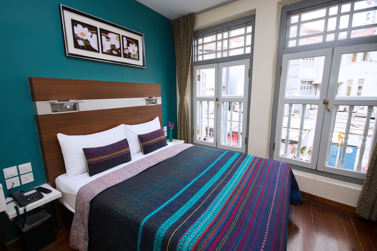 A hotel room with a large bed, a nightstand with a phone, and a window with a view of buildings.