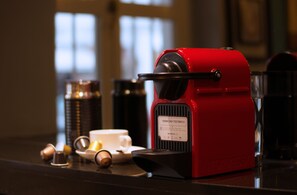 Una cafetera expreso roja sobre una encimera con una taza y un platillo, un plato pequeño y un recipiente con cápsulas de café.