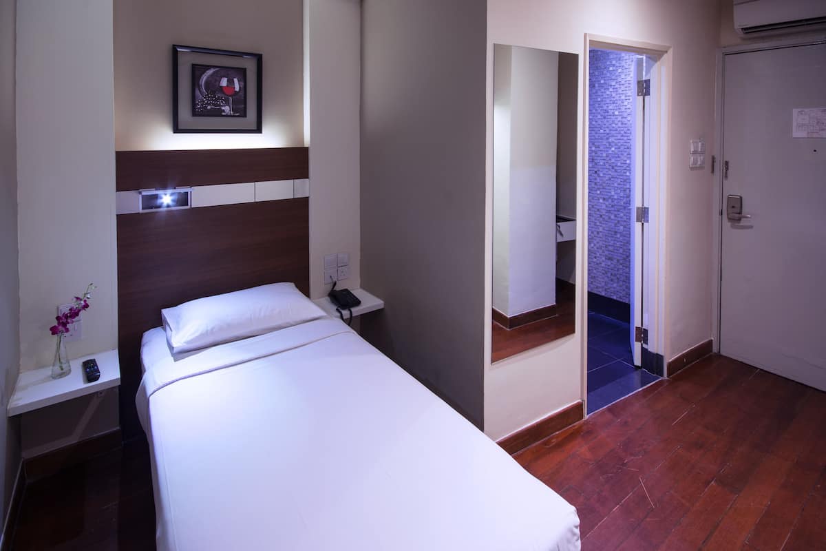 A hotel room with a bed, bedside table, a framed picture, a vase with flowers, a mirror, and a door leading to another room.