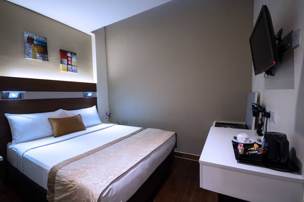 A hotel room with a bed, a desk with a coffee maker, and a TV mounted on the wall.