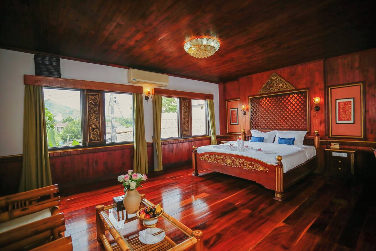 Une chambre traditionnelle en bois, dotée d’un grand lit, d’une table à manger agrémentée d’un vase de fleurs et offrant une vue sur la verdure environnante.