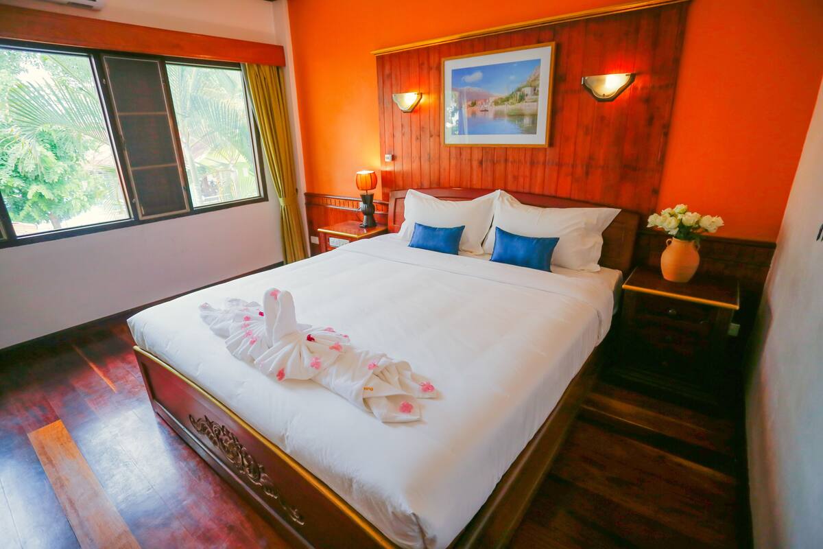 Une chambre d’hôtel avec un grand lit, une tête de lit en bois, une table de chevet avec une lampe, un vase de fleurs et un tableau au mur.