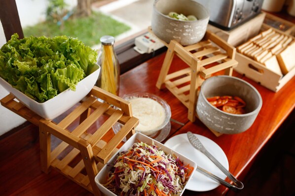 Una mesa con diversos alimentos, entre ellos un tazón de ensalada, un tazón de vegetales cortados y un recipiente con salsa.