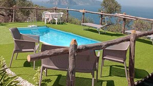 Une piscine avec vue sur la mer et les montagnes, entourée de clôtures en bois et de chaises.