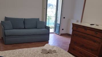 Quarto com cama, sofá, cômoda e porta que dá para uma varanda.