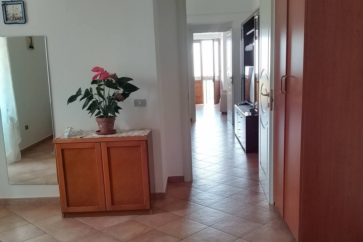 Une pièce avec un sol carrelé, un meuble en bois orné d’une plante en pot, une armoire et un miroir au mur.