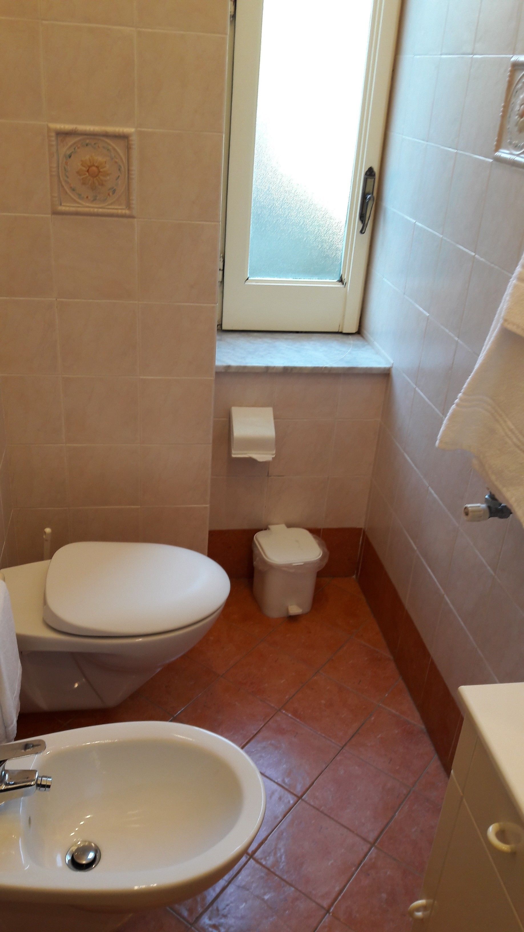 A small bathroom with a toilet, sink, and window.
