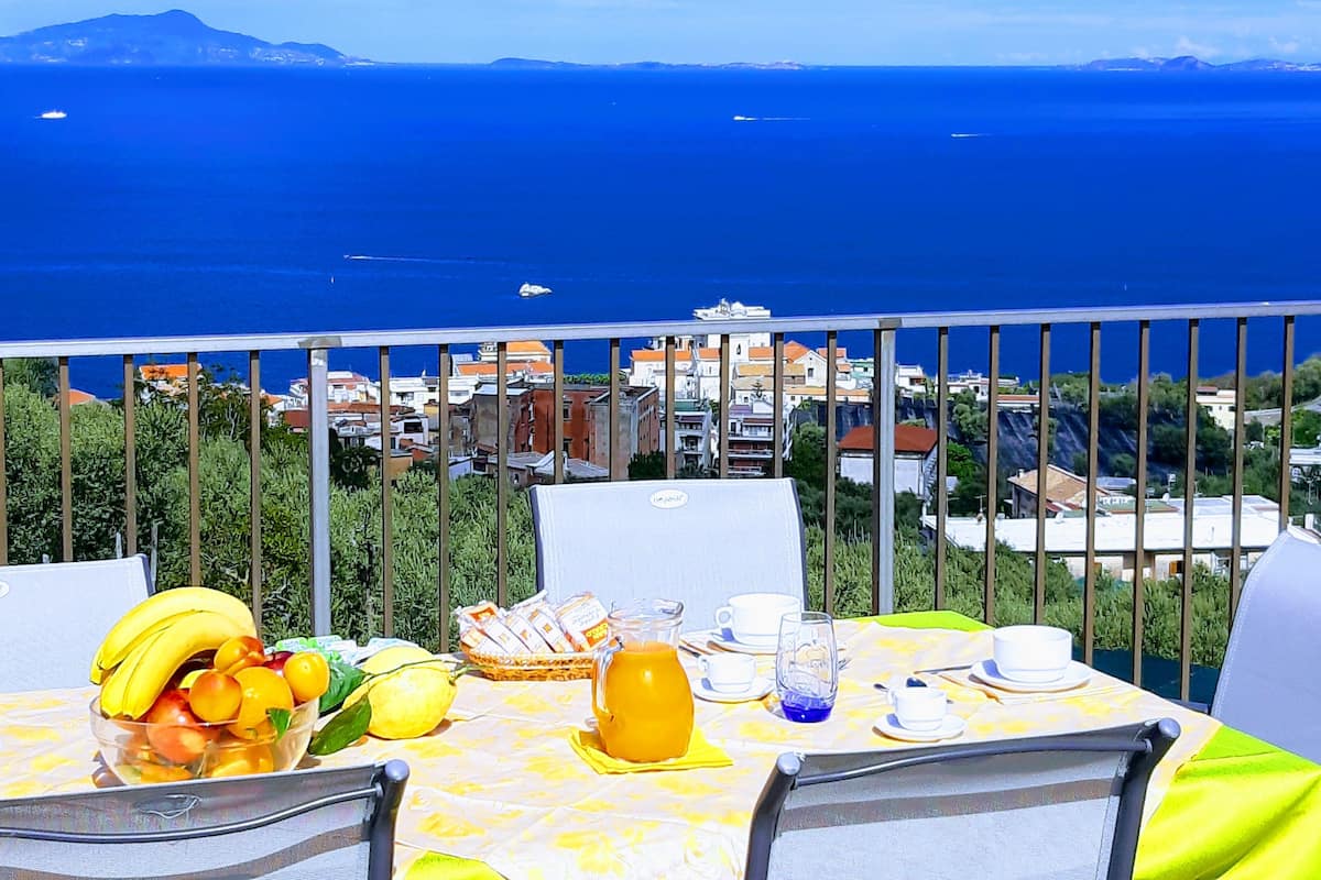 Une table dressée avec des aliments pour le petit-déjeuner, offrant une vue sur la mer et les bâtiments.