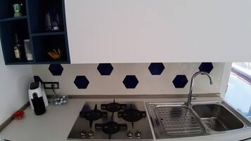 Una cocina con estufa a gas, un fregadero y un estante azul con utensilios de cocina.