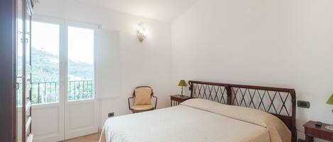 Un dormitorio con una cama grande, una silla, una mesita de noche y una ventana que ofrece vistas al exterior.