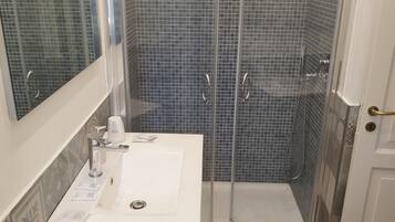 Un baño con un lavamanos blanco, cabina de ducha de vidrio y pared de ducha con azulejos.