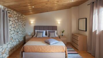 Une chambre avec un mur en pierre, un plafond en bois, un lit recouvert d’une courtepointe, des tables de chevet avec des lampes et une table de nuit ornée d’un vase.