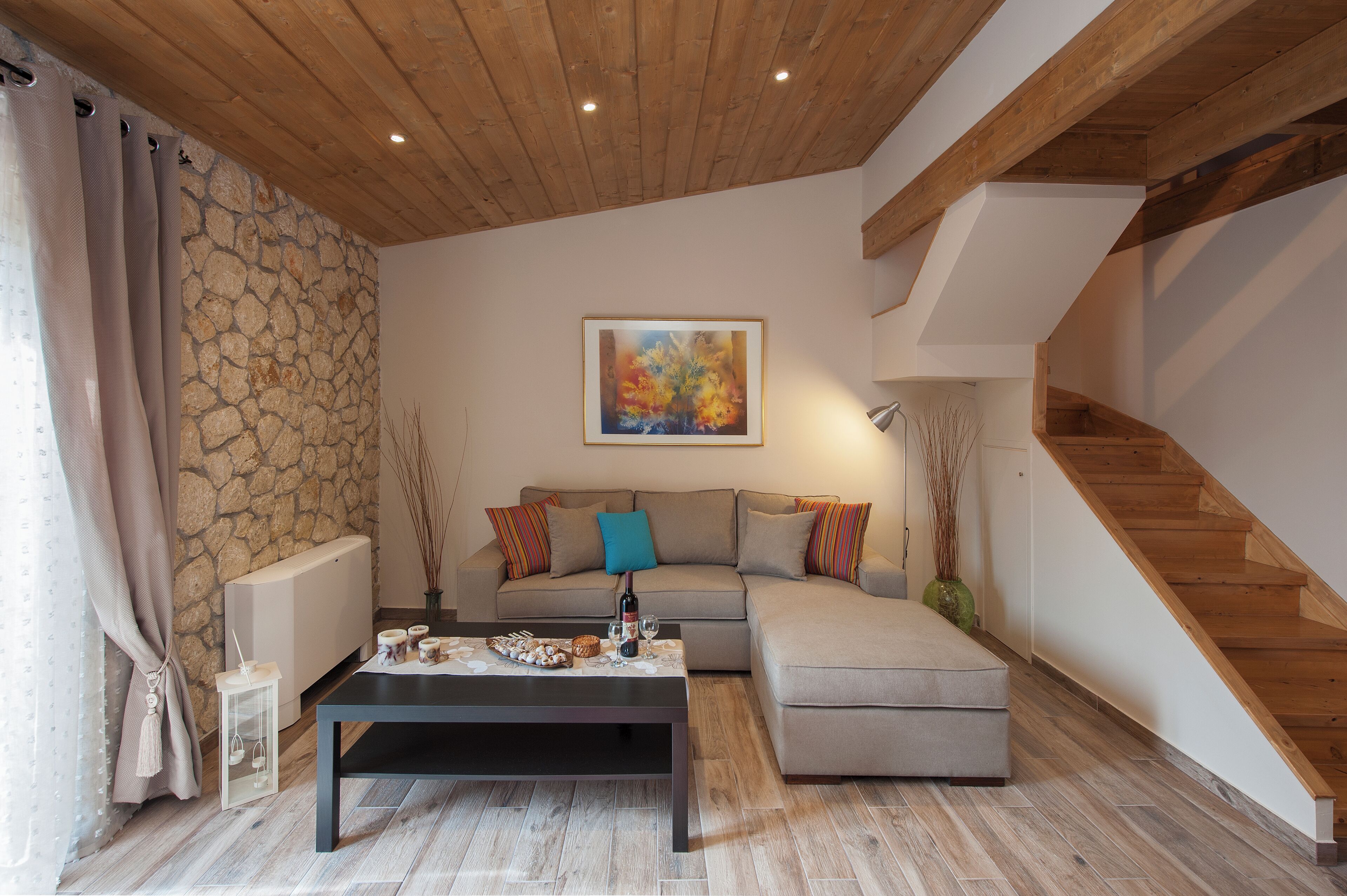 A modern living room with a stone wall, wooden ceiling, a sofa, a coffee table, and a staircase.