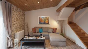 A modern living room with a stone wall, wooden ceiling, a sofa, a coffee table, and a staircase.