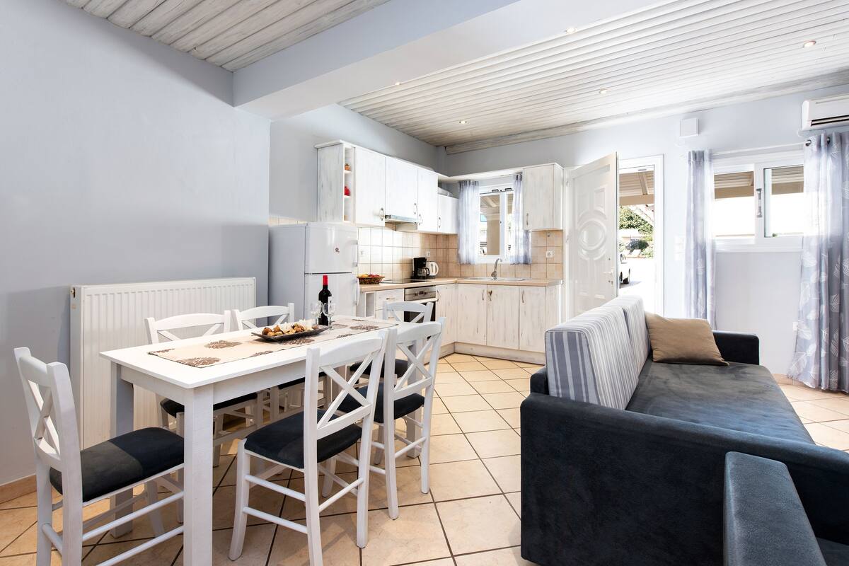 A modern kitchen with white cabinets, a dining table with chairs, and a dark-colored sofa.
