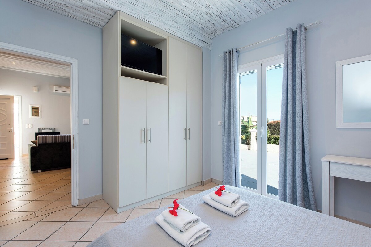 A bedroom with a bed, a wardrobe, a TV, and a balcony with curtains.