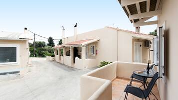 Un edificio residencial con un patio empedrado, una pequeña mesa con sillas y una puerta con ventana.