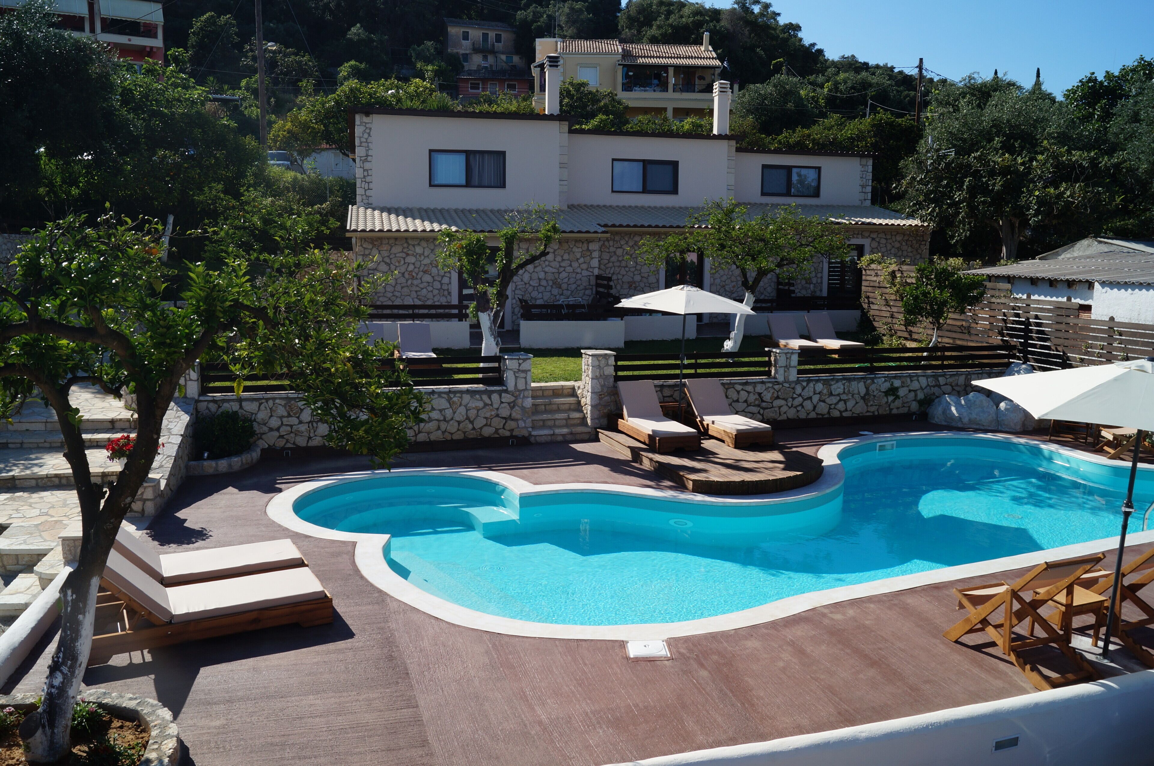A swimming pool with lounge chairs and umbrellas, surrounded by stone walls and a stone pathway.