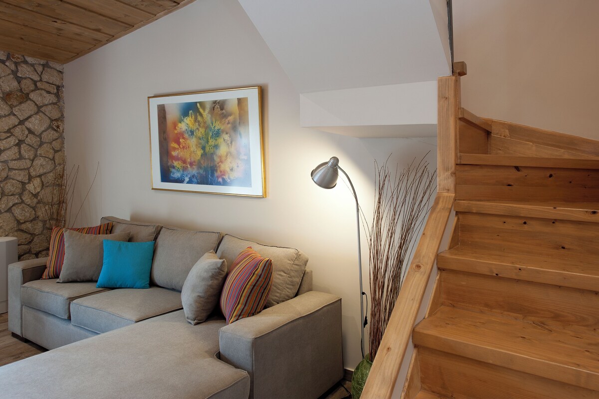 A living room with a sofa, a framed abstract painting, a lamp, and a wooden staircase.