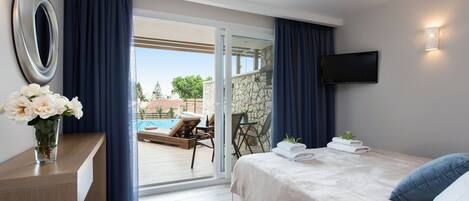 Habitación de hotel con cama, un escritorio con un florero, televisor montado en la pared y vistas a una piscina al aire libre.