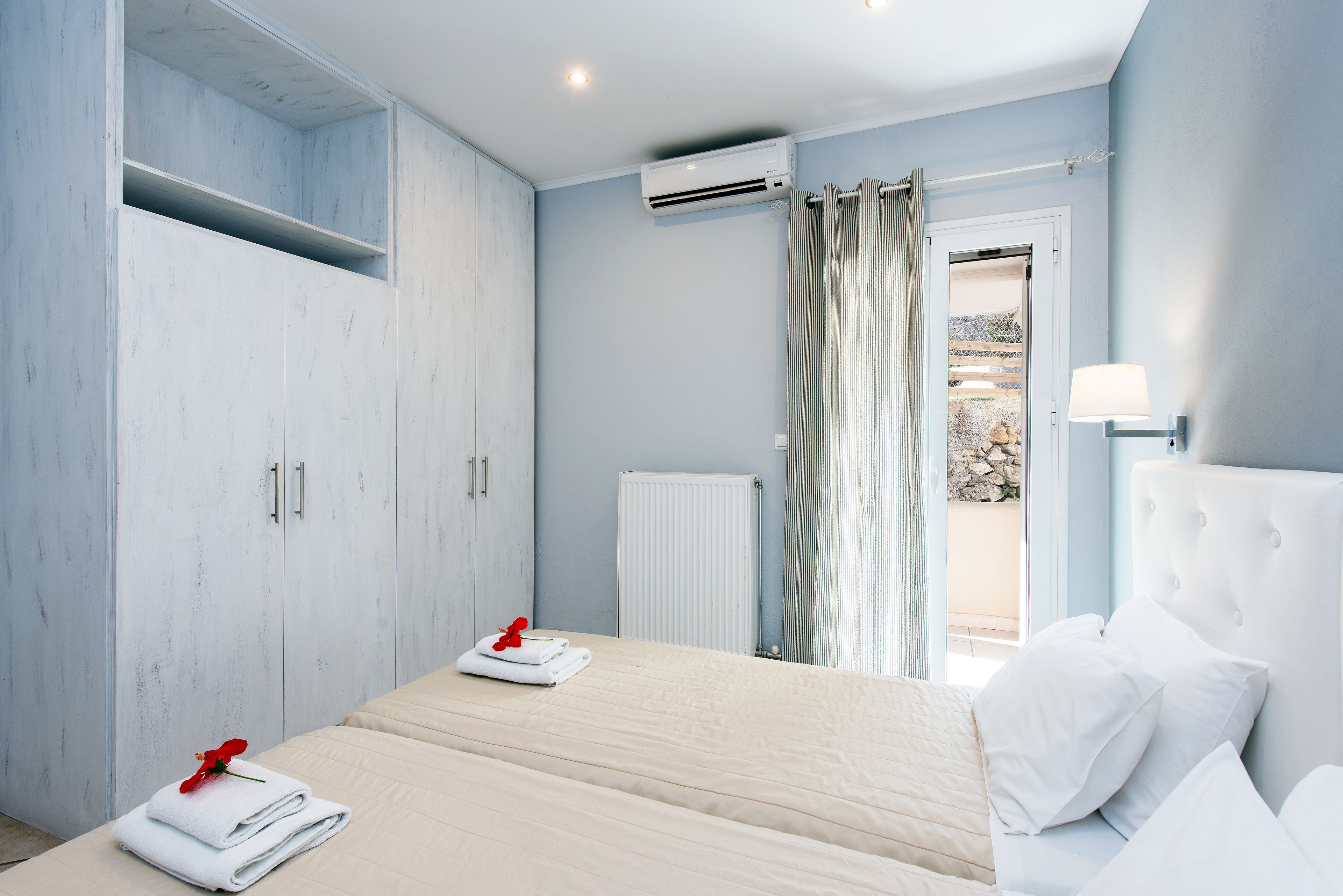 A bedroom with a bed, a wardrobe, an air conditioning unit, a radiator, and a view through a door.