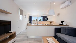 Una sala de estar moderna con televisor, sofá y mesa de centro. Hay una zona de cocina con pileta y mostrador.