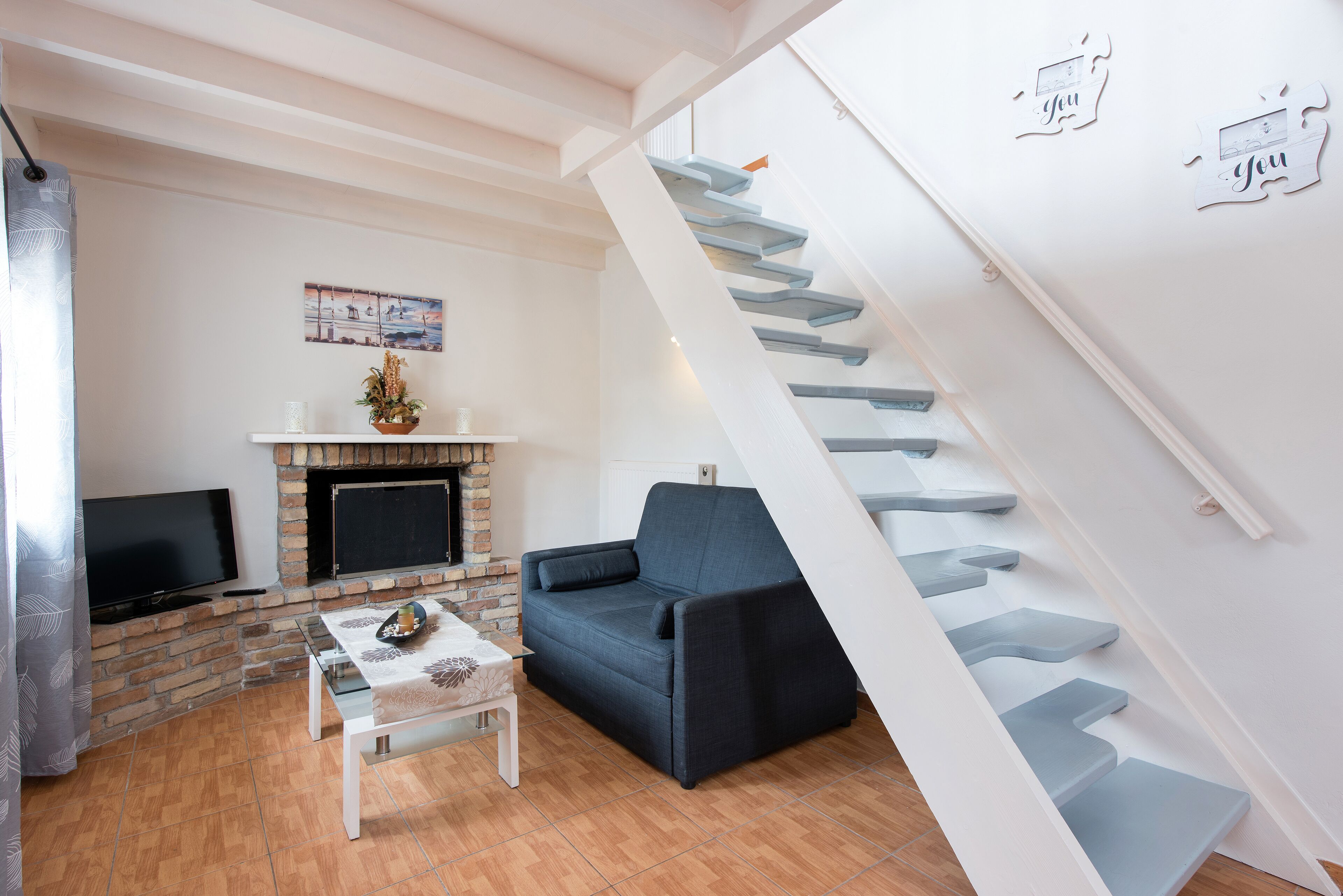 Una sala de estar con un sofá, televisión, chimenea y escalera.