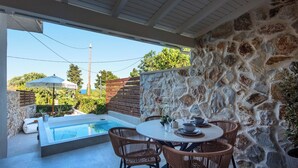 Zona junto a la piscina con un muro de piedra, una mesa redonda con sillas y vista al mar.