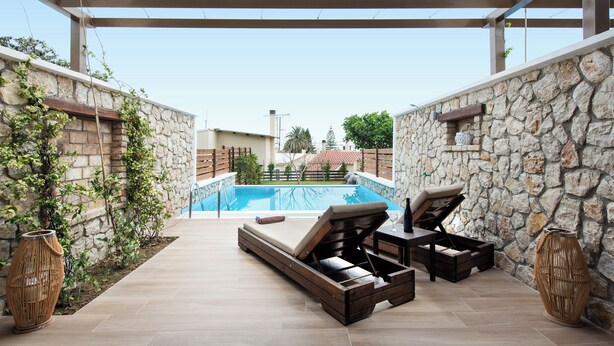 Un área de piscina al aire libre con muros de piedra, una tumbona de madera y una pérgola.