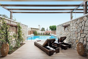 Un área de piscina al aire libre con muros de piedra, una tumbona de madera y una pérgola.