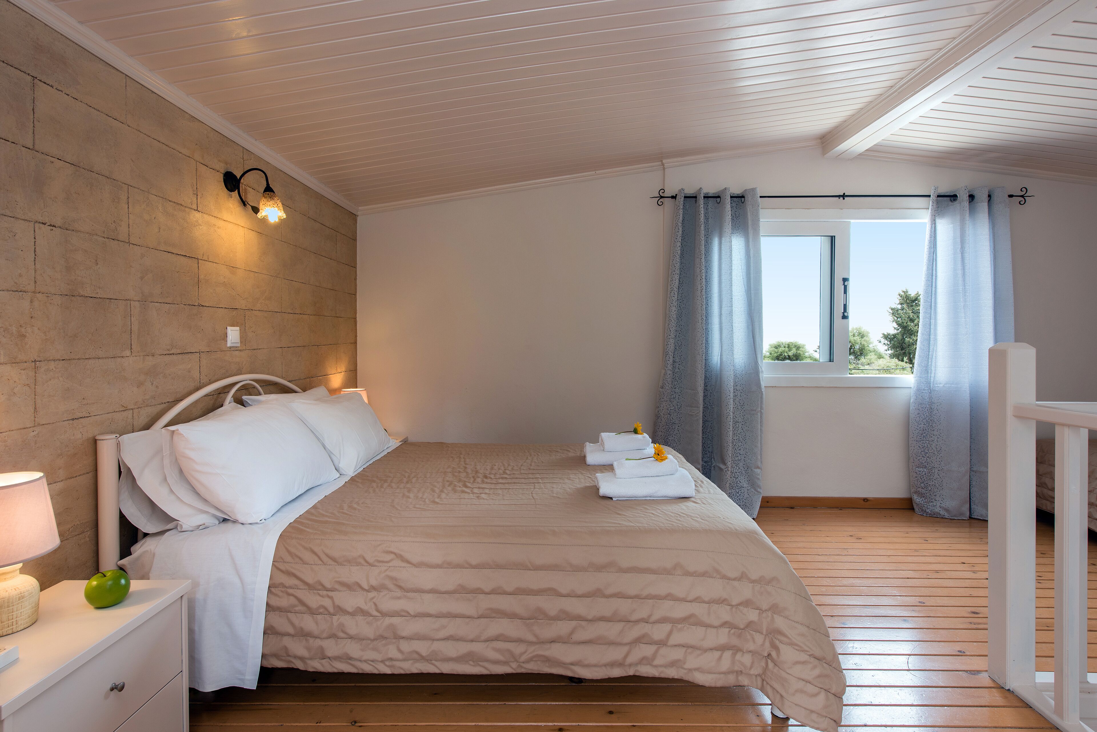A neatly made bed with white linens, a bedside lamp, and a green apple on a nightstand.