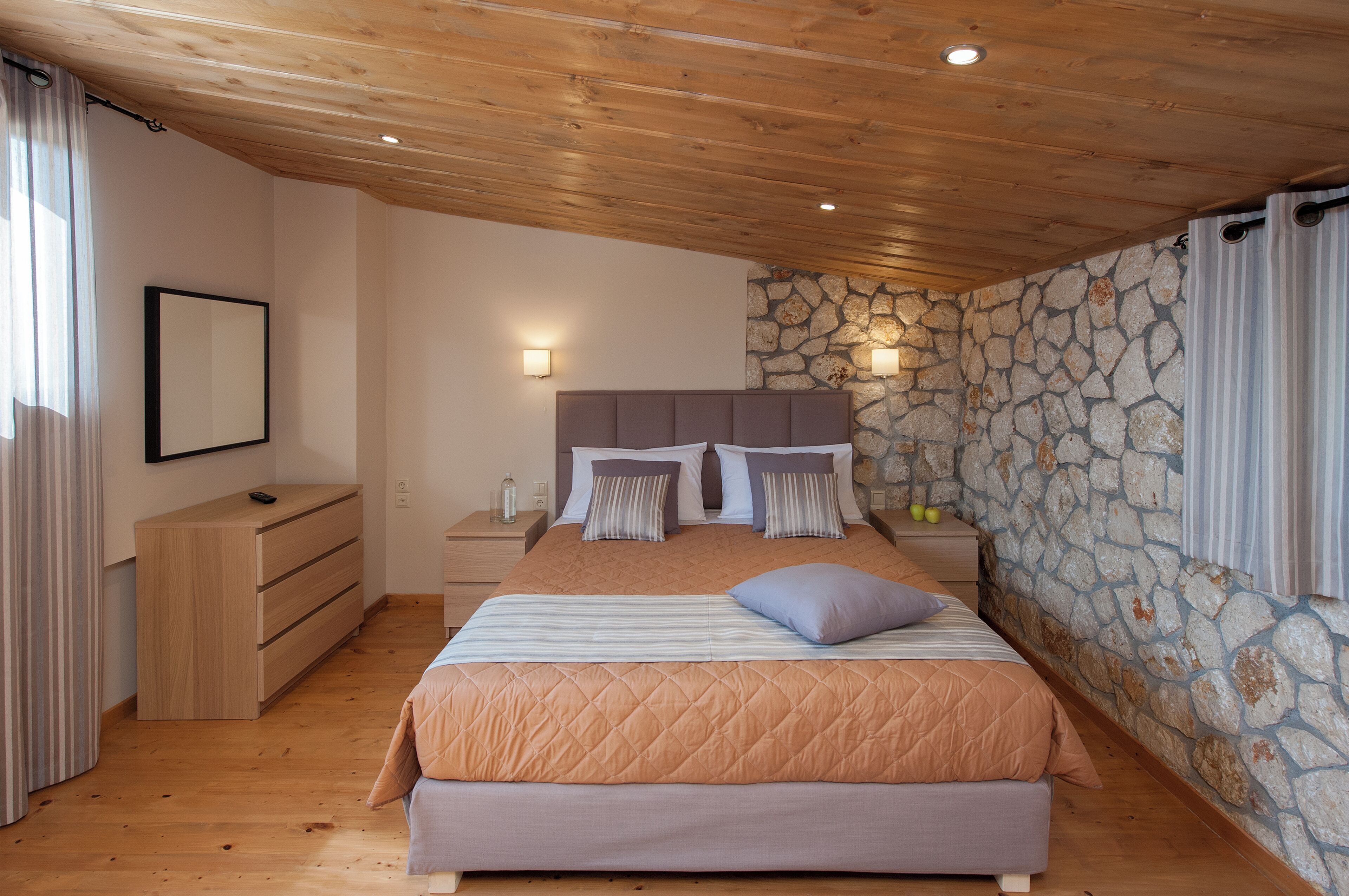 Une chambre à coucher avec un lit, une tête de lit en bois, un mur en pierre et une table de chevet avec une lampe.
