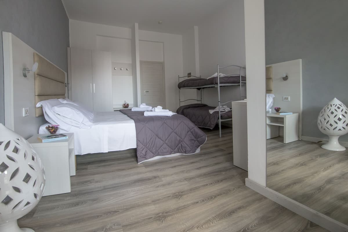 A bedroom with a bunk bed, a single bed, a bedside table with a lamp, a mirror, and a wardrobe.