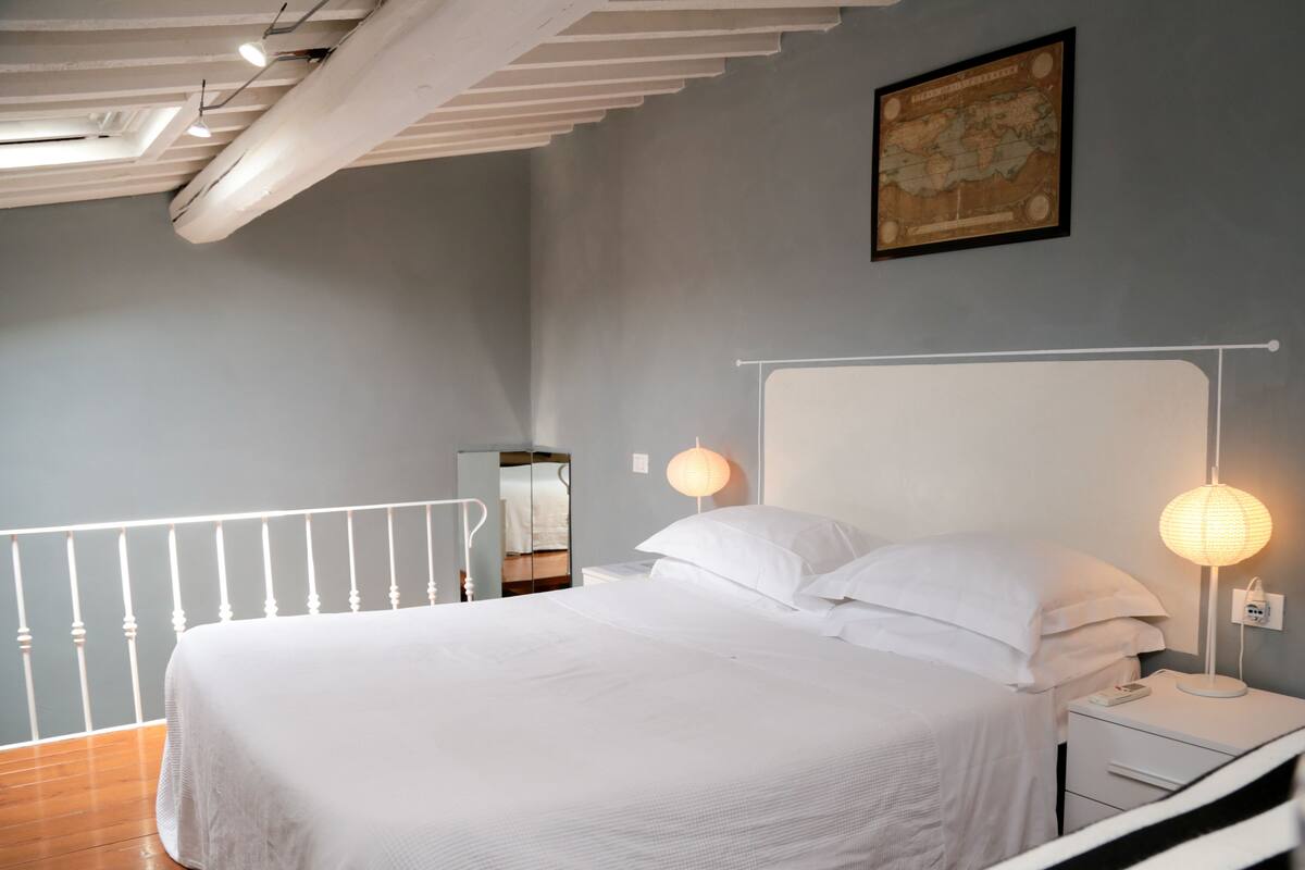A bedroom with a bed, bedside table, lamp, and a map on the wall.