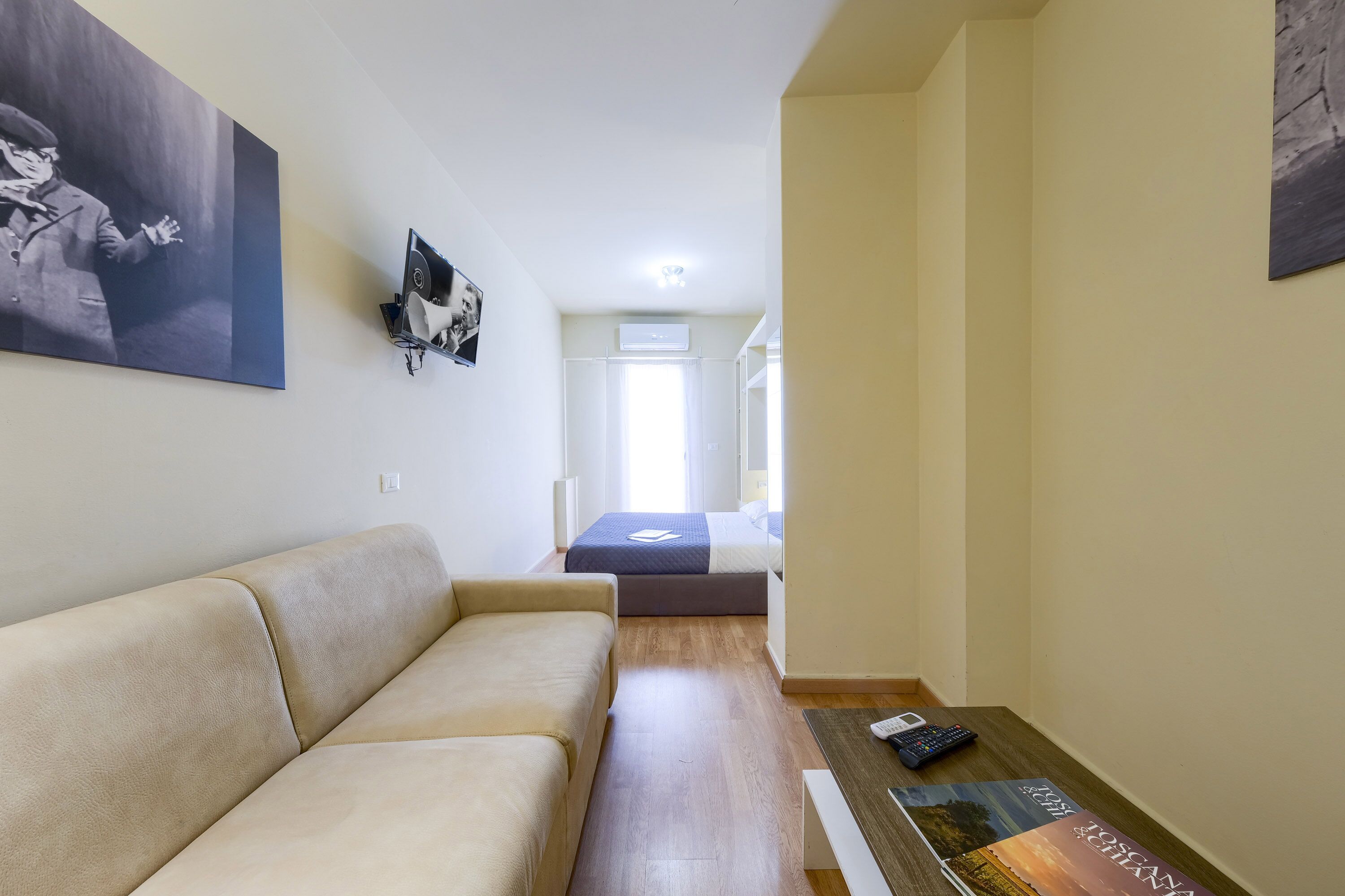 Une chambre d’hôtel moderne avec un canapé beige, une table basse en bois et un lit en arrière-plan.