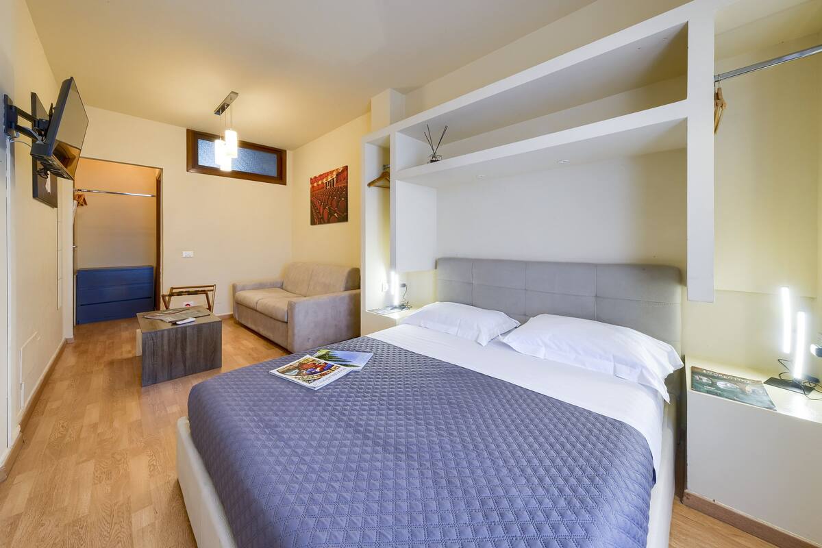 A hotel room with a large bed, a sofa, a small table, and a desk with a lamp.