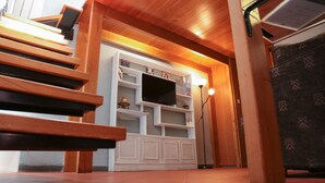 Una escalera de madera que lleva a una sala de estar con televisor y estanterías.