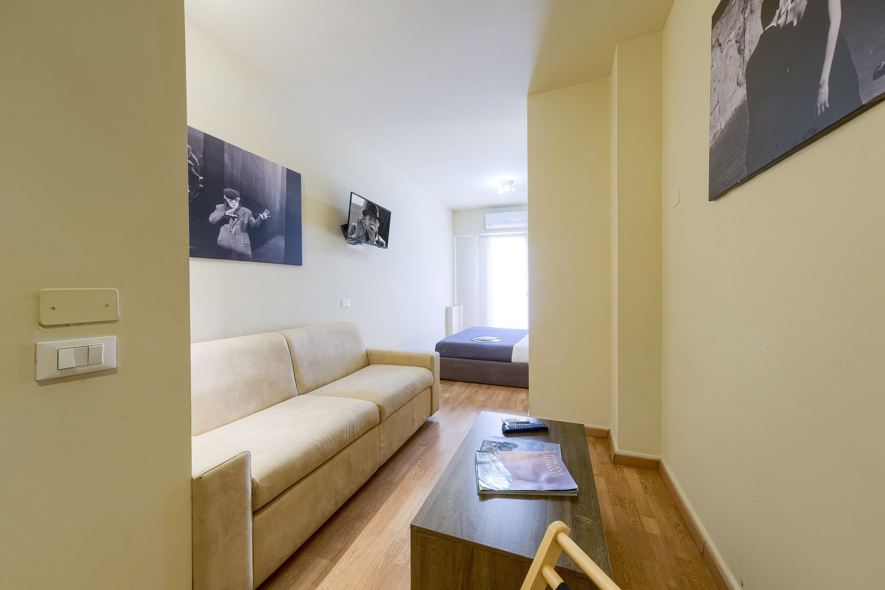 Ein Wohnzimmer mit einem beigefarbenen Sofa, einem Holztisch und einem kleinen, an der Wand montierten Fernseher.