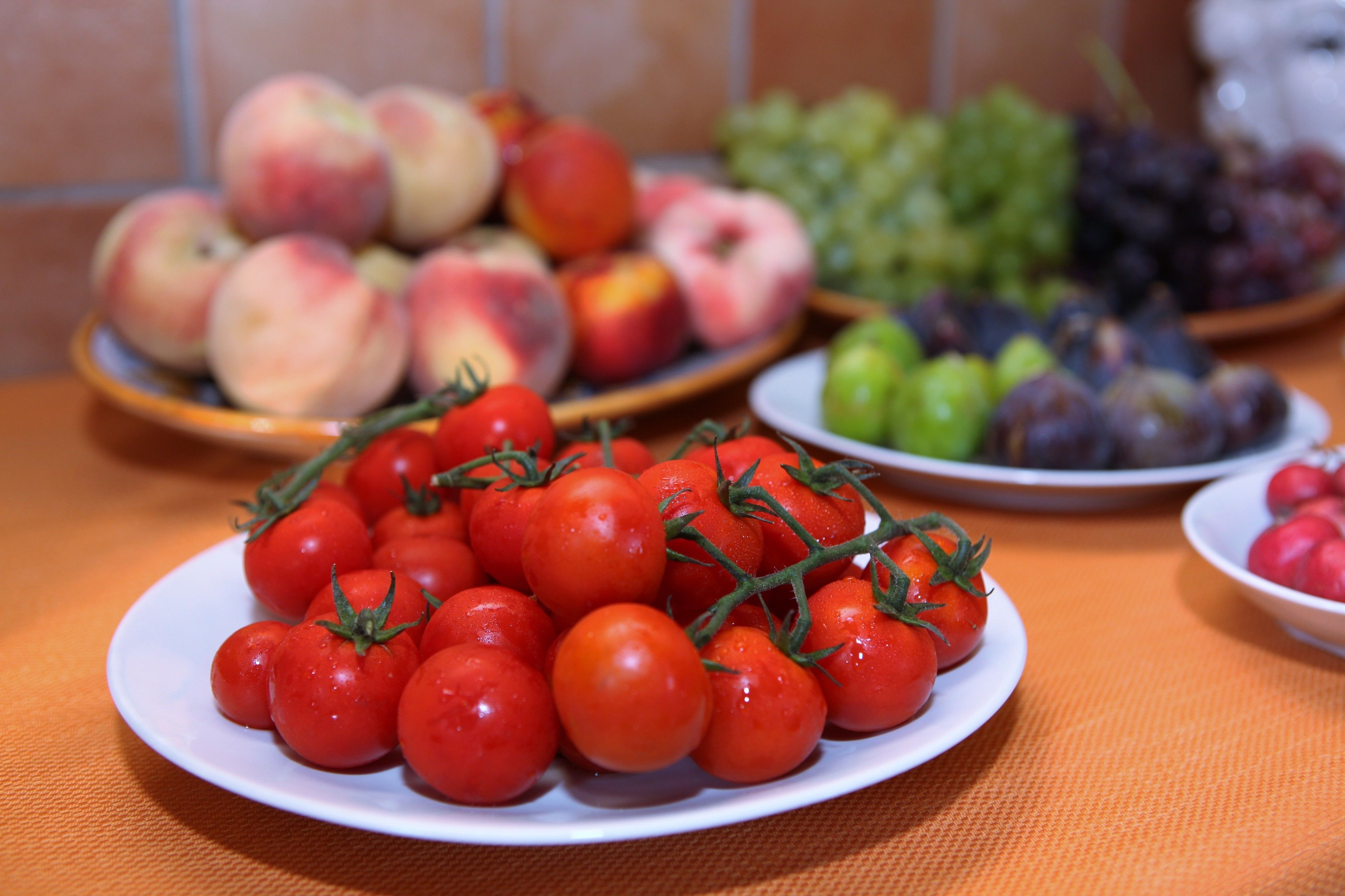 A table with various fruits including tomatoes, peaches, grapes, and apples.