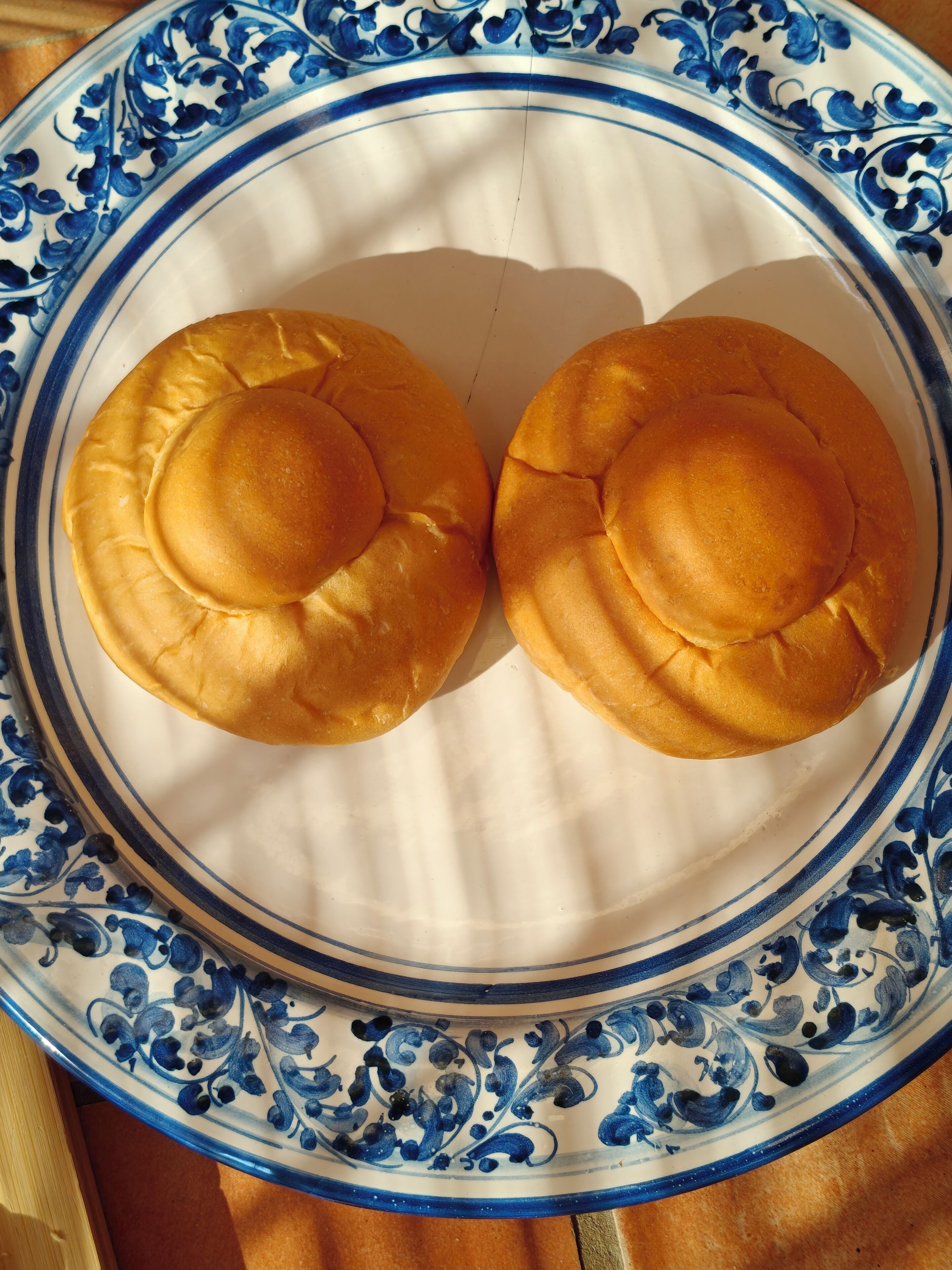 Two round, golden-brown baked goods on a white plate with blue floral patterns.