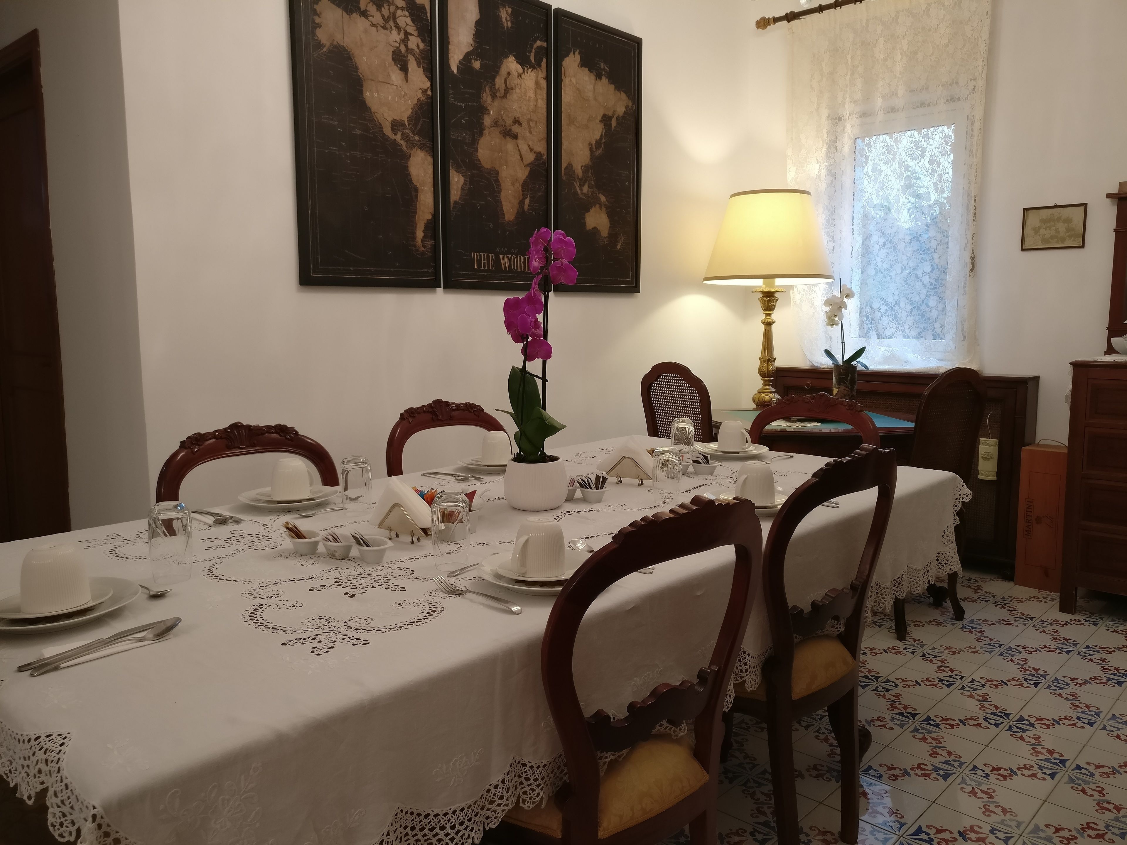 Zona pranzo con tavolo apparecchiato per quattro, una mappa del mondo appesa al muro e una lampada.