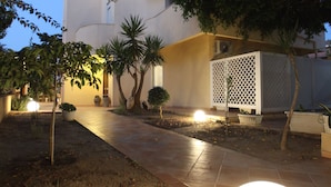Un patio con un sendero, plantas en macetas y una lámpara esférica.