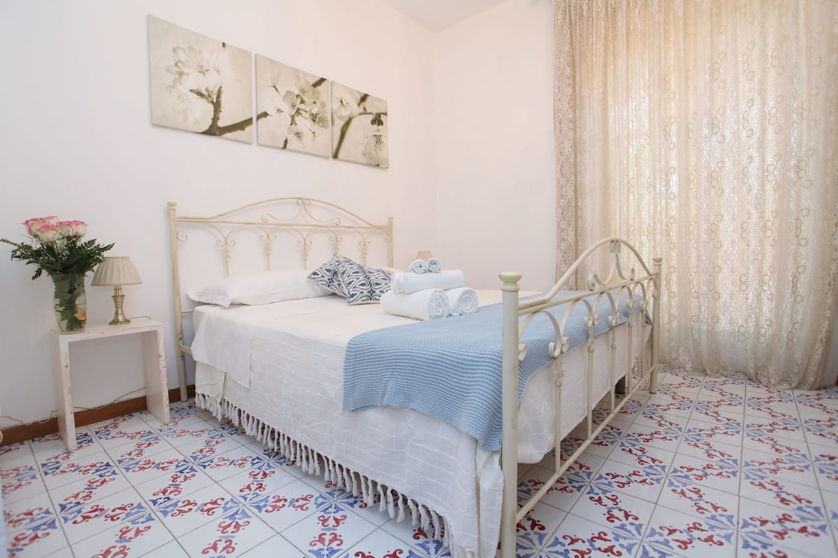 Une chambre à coucher avec un lit, une table de chevet, une lampe et un vase de fleurs.