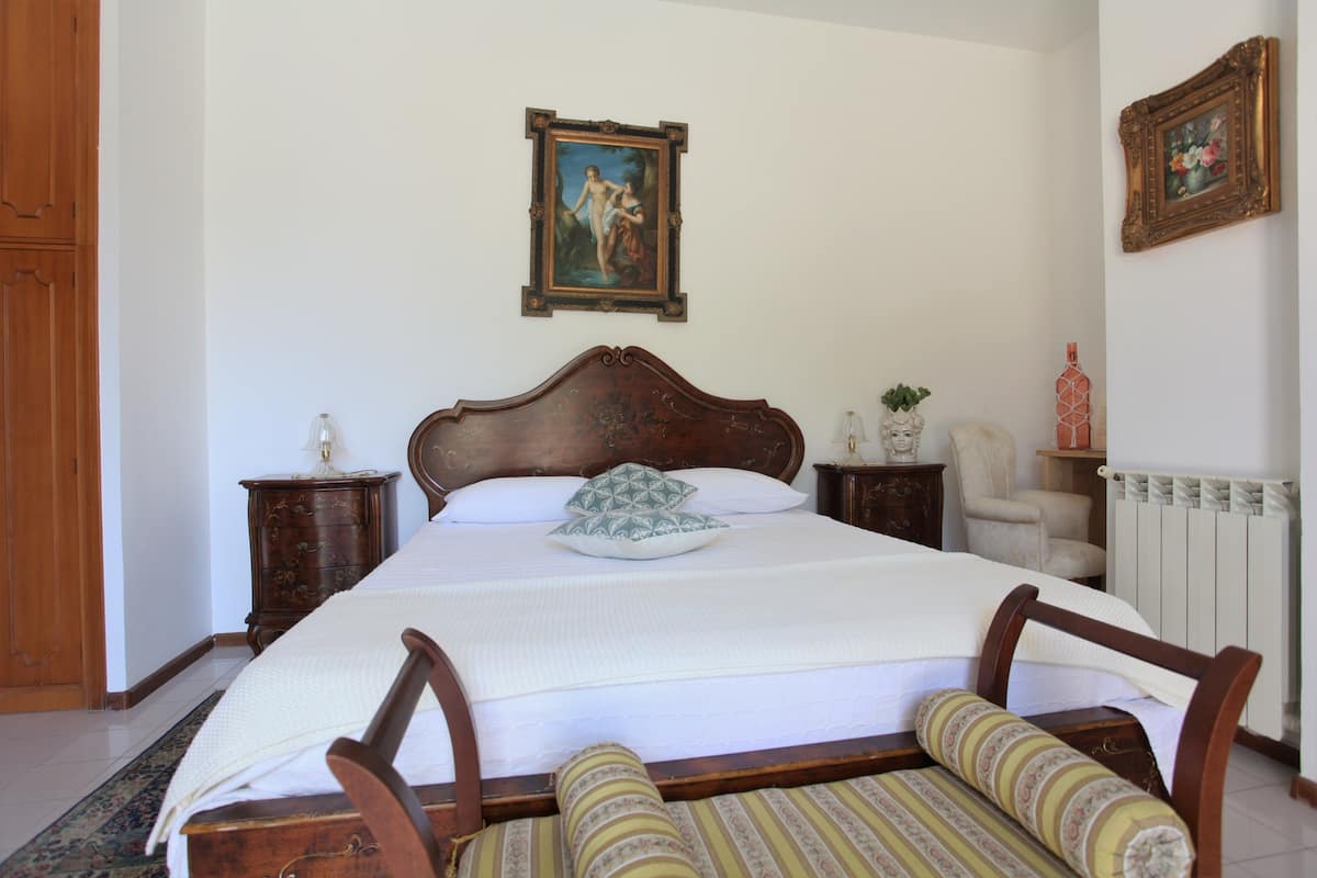 Une chambre à coucher avec un grand lit, une tête de lit en bois, une table de chevet, une chaise, une commode et un tableau accroché au mur.
