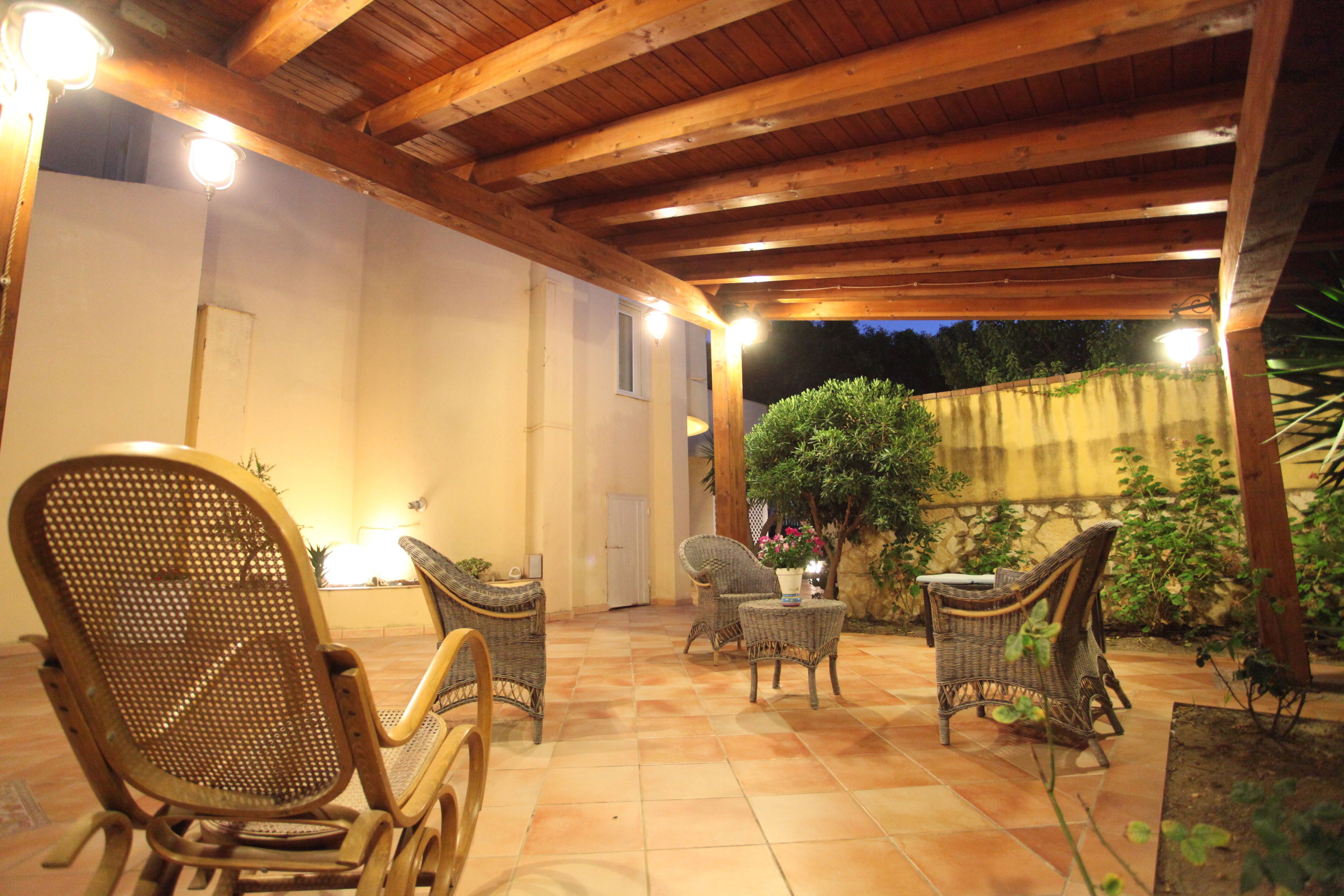 Un patio al aire libre con vigas de madera en el techo, mobiliario de mimbre y plantas en macetas.