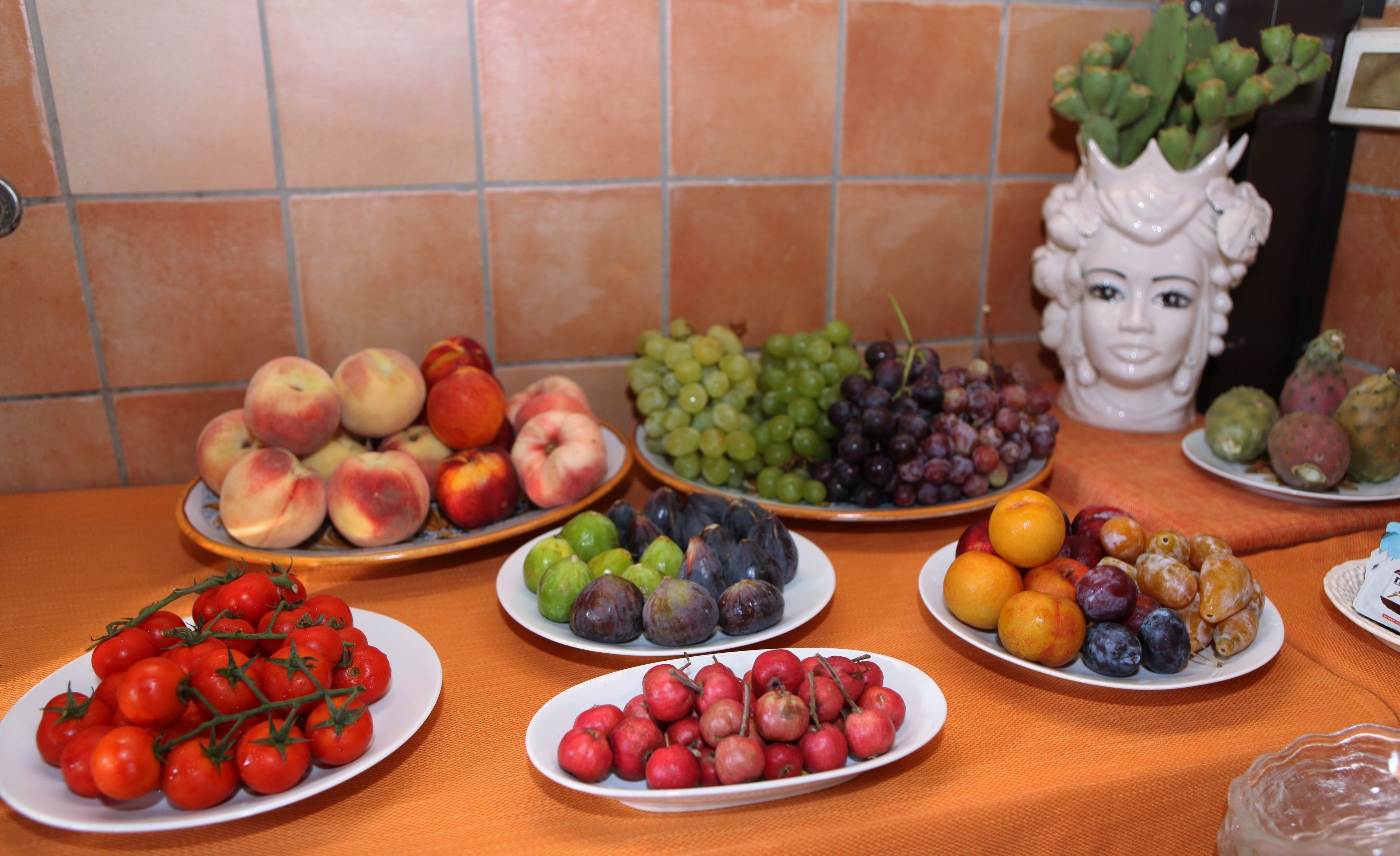 Una mesa con diversas frutas y verduras, entre ellas, tomates, uvas y melocotones.