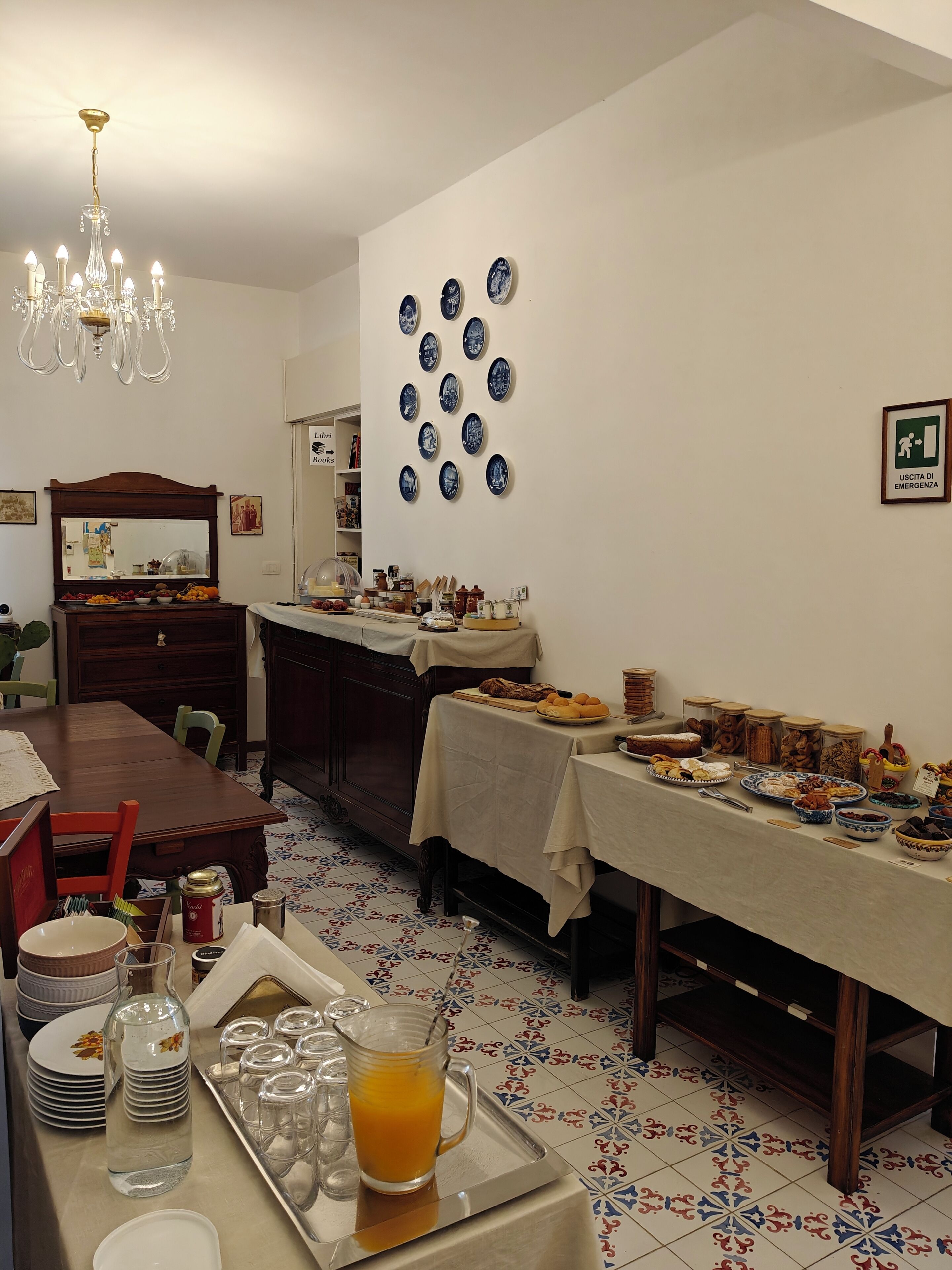 Un comedor con una mesa larga cubierta con mantel, varios platos y una bandeja con vaso de jugo de naranja.