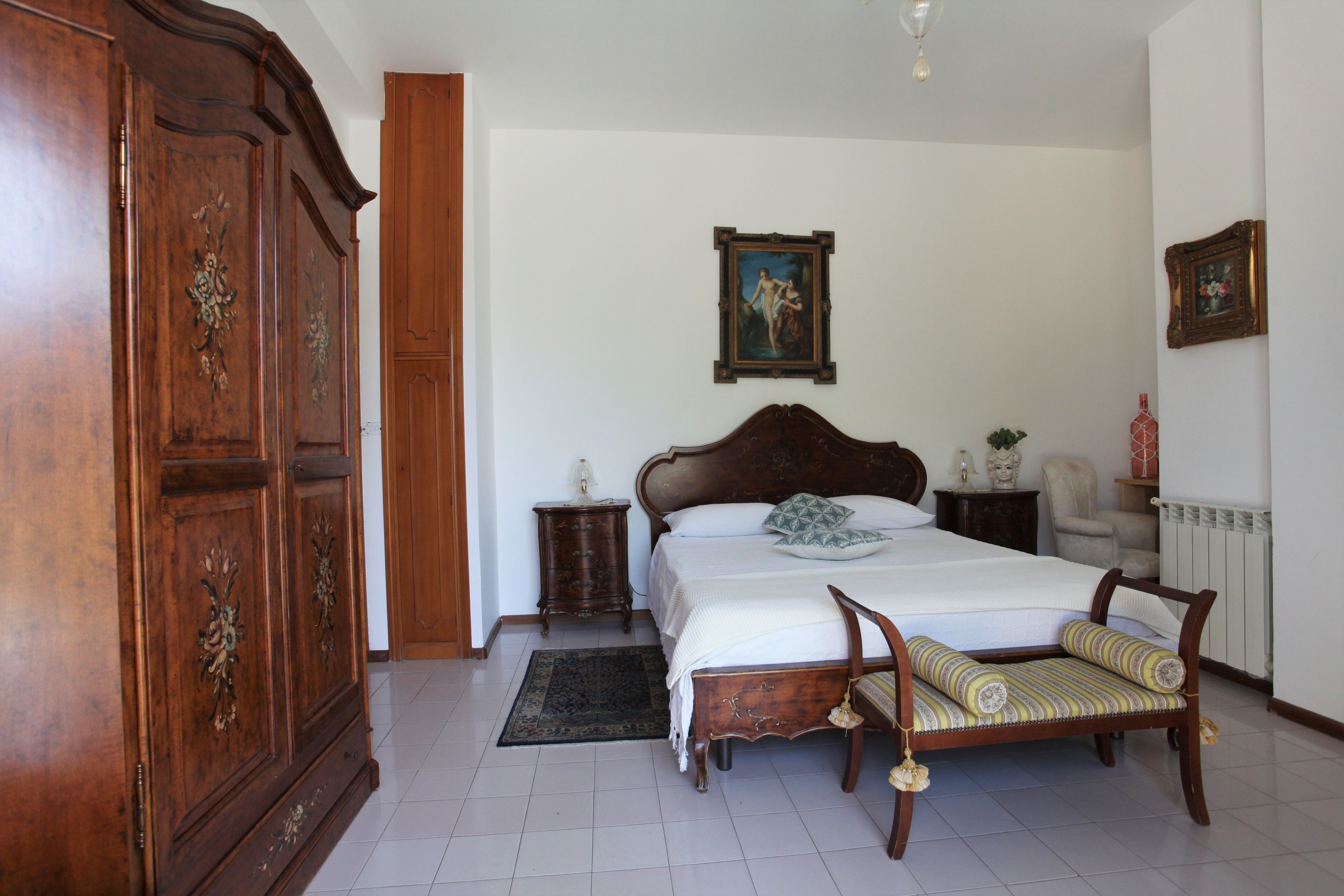 Une chambre à coucher avec une grande armoire en bois, un lit avec une tête de lit en bois, une table de chevet, une chaise et un tableau accroché au mur.